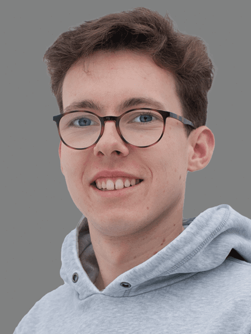 Portr&auml;t eines jungen Mannes mit Brille, l&auml;chelnd, in einem grauen Hoodie vor grauem Hintergrund.