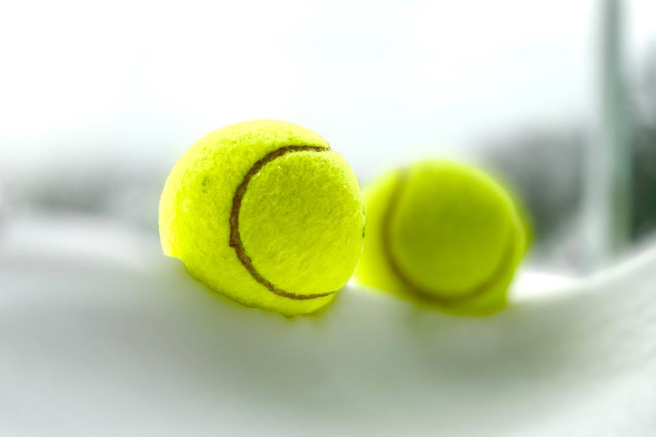 Nahaufnahme von zwei gelben Tennisbällen auf einem weißen Tisch. Hintergrund leicht unscharf.